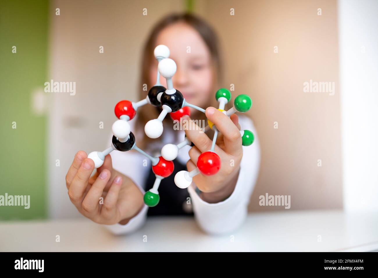 una niña muy joven con peto negro se sienta en su habitación y aprende  sobre un modelo para moléculas Fotografía de stock - Alamy