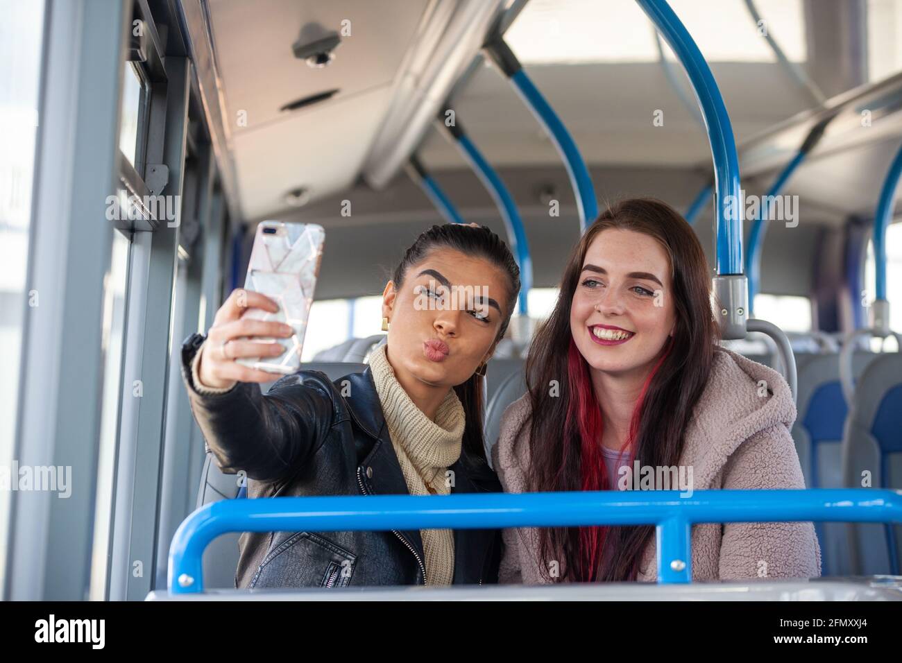 Dos mujeres jóvenes tirando de caras y tomando una selfie de ellos mismos dentro de un autobús Foto de stock