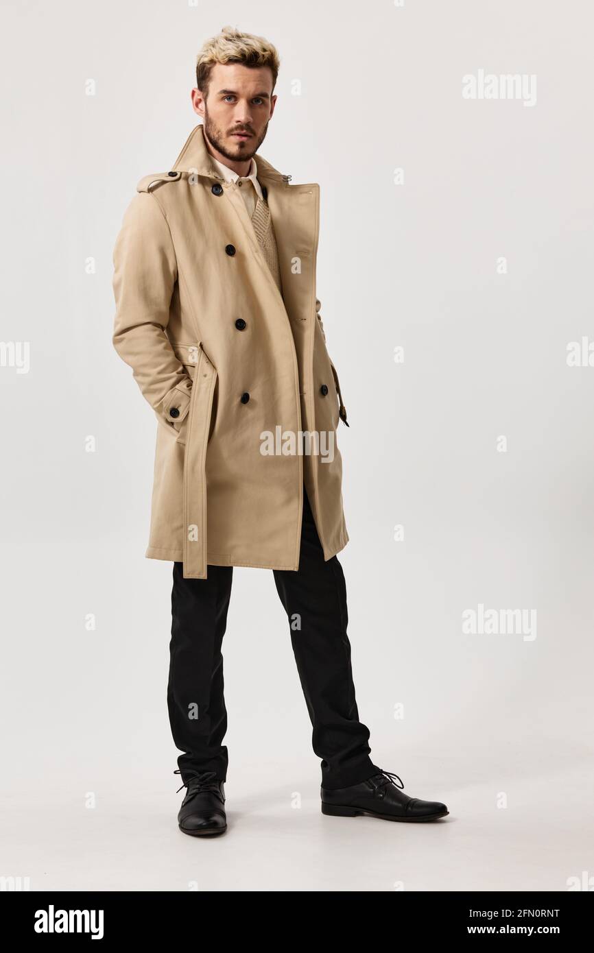 hombre en beige abrigo pantalones y botas posando en un fondo claro  Fotografía de stock - Alamy