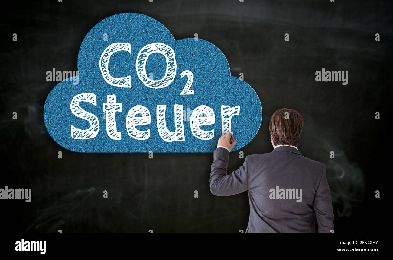Businessman pinta CO2 Steuer (en el impuesto alemán al carbono) en pizarra con tiza. Foto de stock