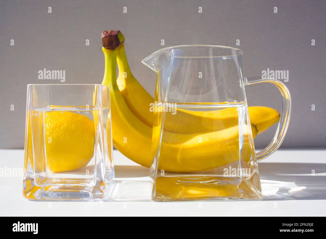 Agua pura en la jarra de cristal y el vaso, frutas amarillas en el fondo. Foto de stock