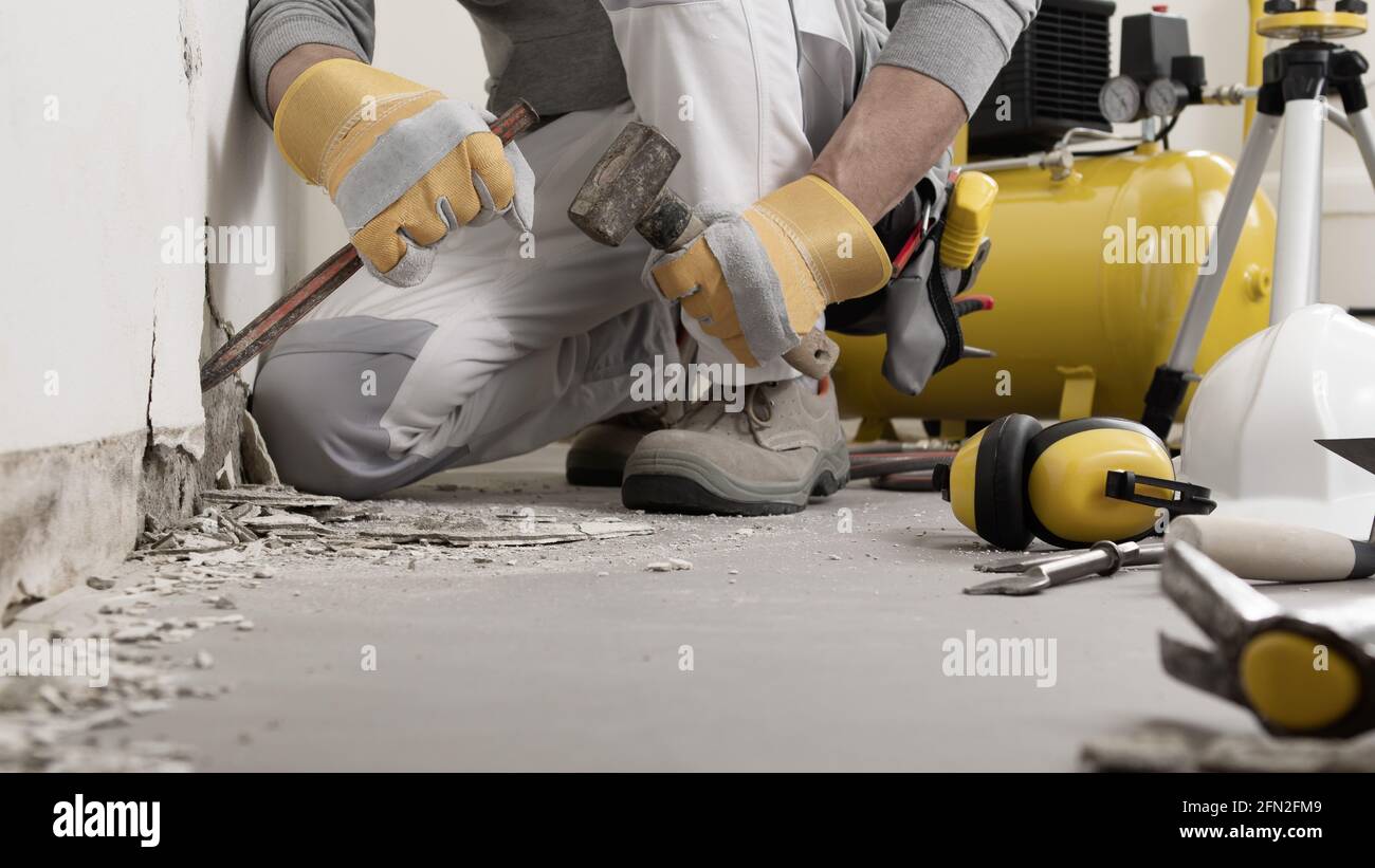 El trabajador de la construcción las manos con guantes que trabajan con  martillo y cincel para quitar el yeso viejo de la pared para la renovación  de la casa, cerca con los
