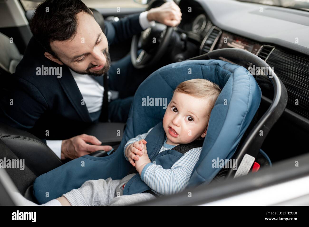 El padre tiende a un niño mientras conduce en el trabajo con un bebé  sentado en un asiento de coche moderno. Niño recién nacido viajando seguro  en la carretera. Una forma segura