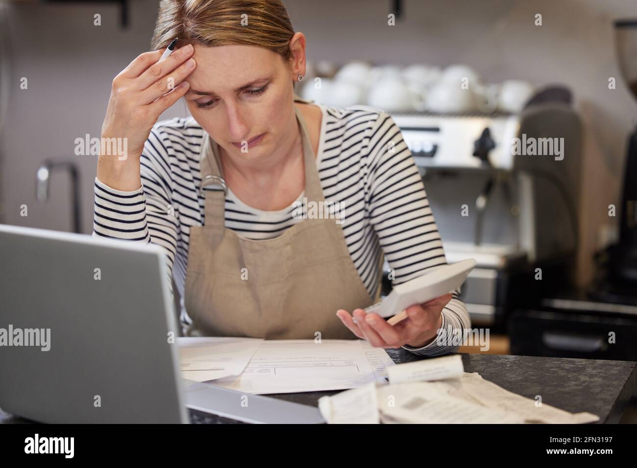 Preocupada mujer propietaria de la cafetería en la búsqueda de dificultades financieras A través de Bills usando el ordenador portátil y la calculadora Foto de stock