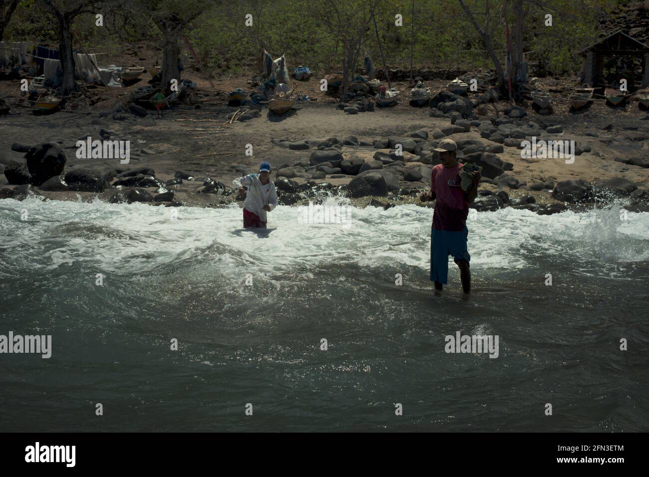 Hombres esperando para ayudar a desembarcar en una embarcación de pesca en la playa rocosa de 'Lamalera B' en la aldea de Lamalera, Isla Lembata, East Nusa Tenggara, Indonesia. Foto de stock