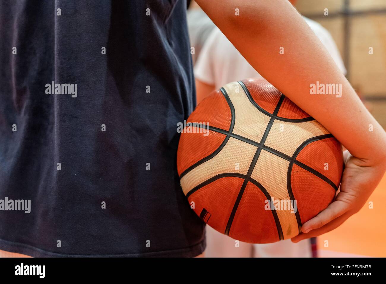 Primer plano en la pelota de baloncesto en manos de un desconocido caucásico niño adolescente que lo sostiene en el entrenamiento o esperando que juego juegue al desarrollo deportivo Fotografía