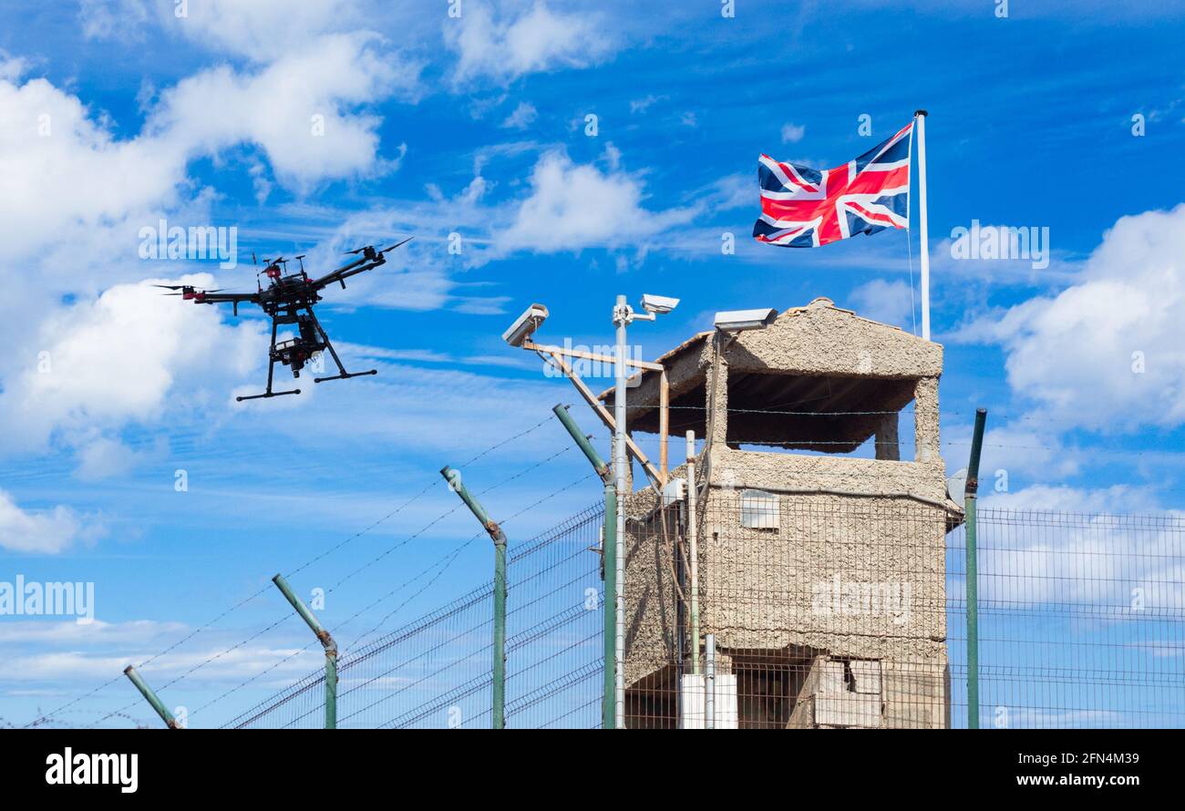 Aviones teledirigidos volando sobre la torre de vigilancia con la bandera de Reino Unido Union Jack volando. Control fronterizo británico, Brexit, inmigración ilegal, centro de detención... concepto Foto de stock