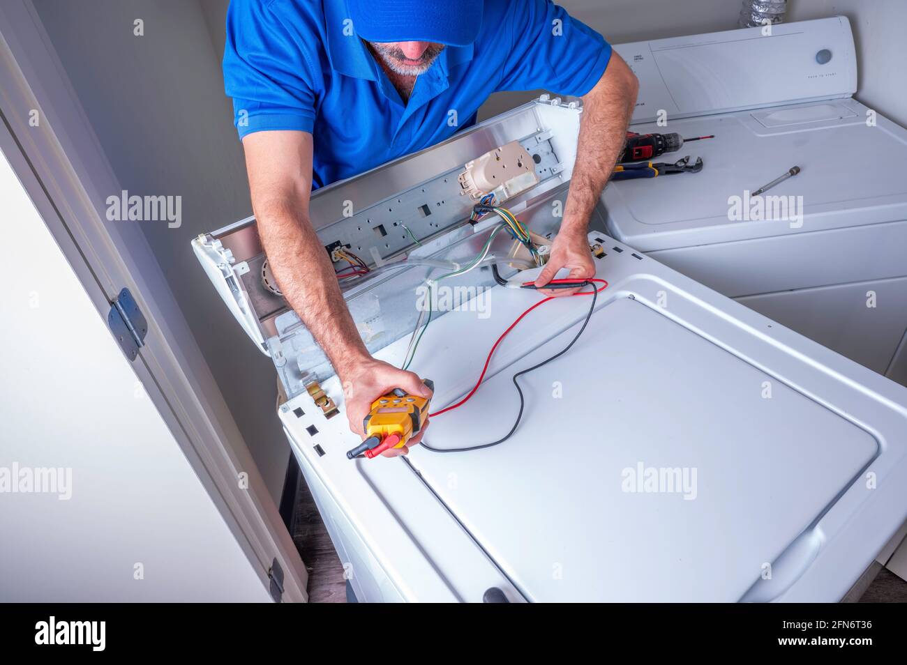 Técnico de electrodomésticos o reparador que trabaja en circuitos de la parte superior cargue la lavadora dentro de una casa residencial Foto de stock