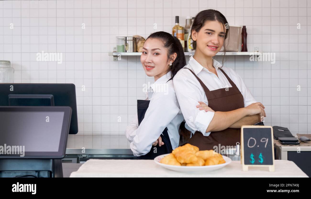 El tendero y el barista sonreían con los brazos doblados delante de una cafetería. Ambiente matutino en una cafetería. Foto de stock