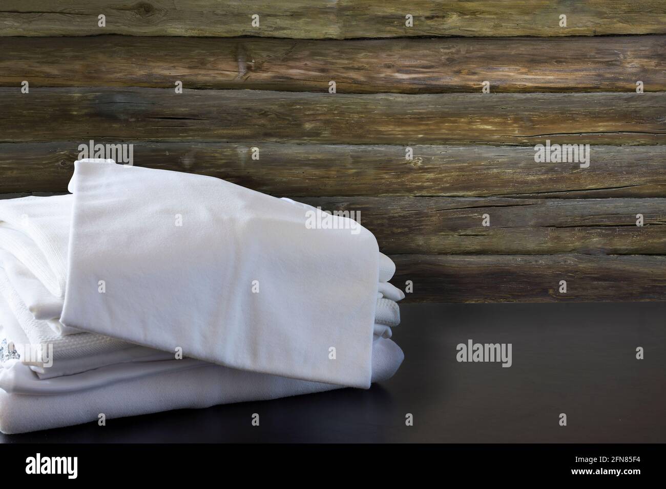 Pila de ropa blanca delante de la pared de madera y sobre el suelo negro. Camisa y camisetas Foto de stock