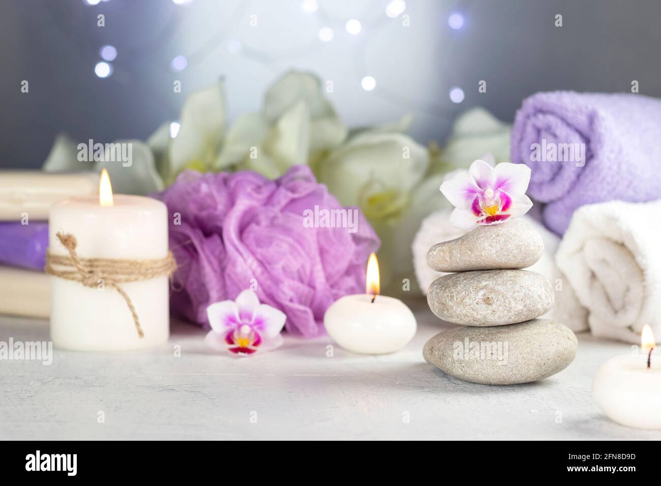 piedras de masaje, velas encendidas, toallas enrolladas, flores, luces  abstractas. Composición terapéutica spa resort en colores lila Fotografía  de stock - Alamy