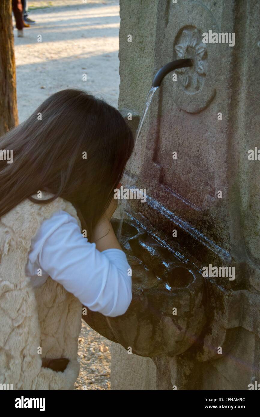 Una niña bebiendo agua dulce en una fuente al aire libre Foto de stock