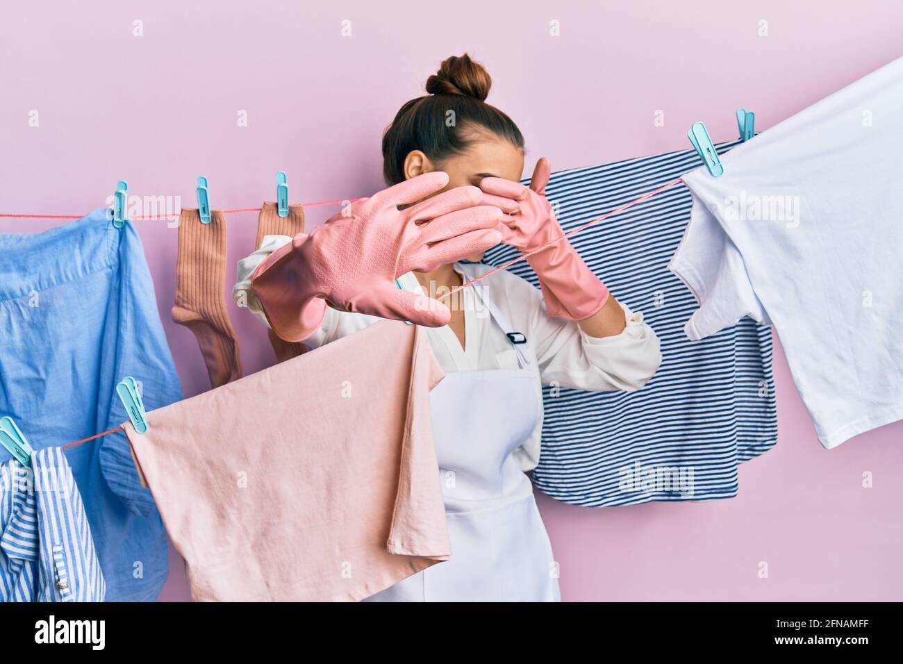 Hermosa morena joven mujer lavando ropa en la línea de la ropa que cubre los ojos con las manos y haciendo gesto de parar con triste y del miedo. Fotografía