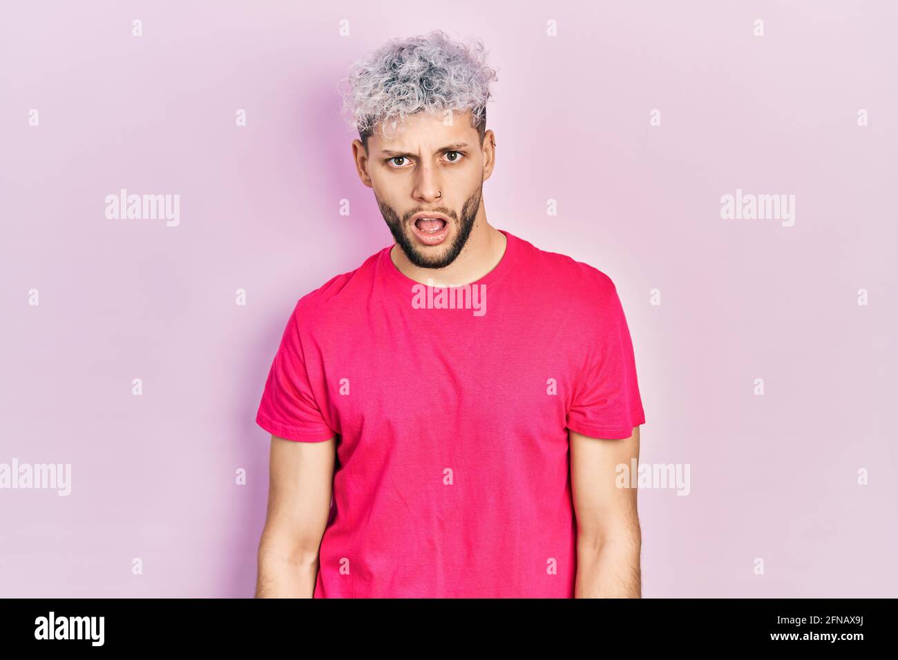 Joven hombre hispano con cabello teñido moderno con camiseta rosa informal  en cara de choque, con un aspecto escéptico y sarcástico, sorprendido con  la boca abierta Fotografía de stock - Alamy