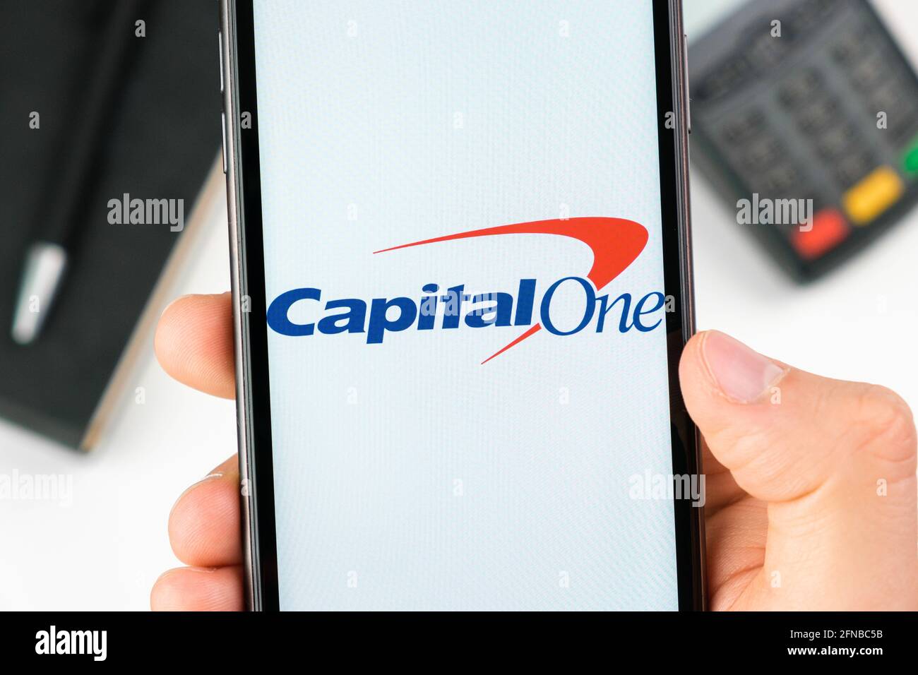 Logotipo de Capital One Bank en la pantalla del smartphone en manos del hombre en el fondo de la terminal de pago, 2021 de mayo, San Francisco, EE.UU Foto de stock