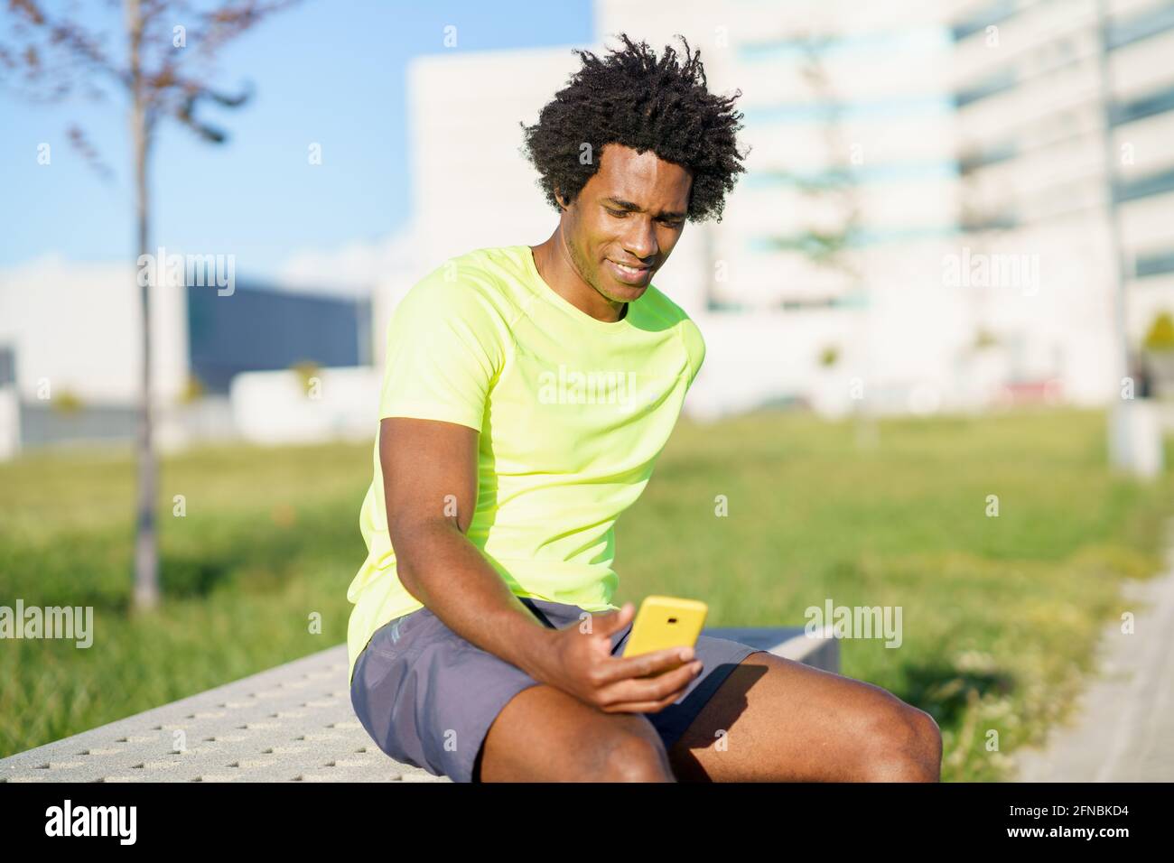 Hombre negro consultando su smartphone con alguna aplicación de ejercicio mientras descansa de su entrenamiento. Foto de stock