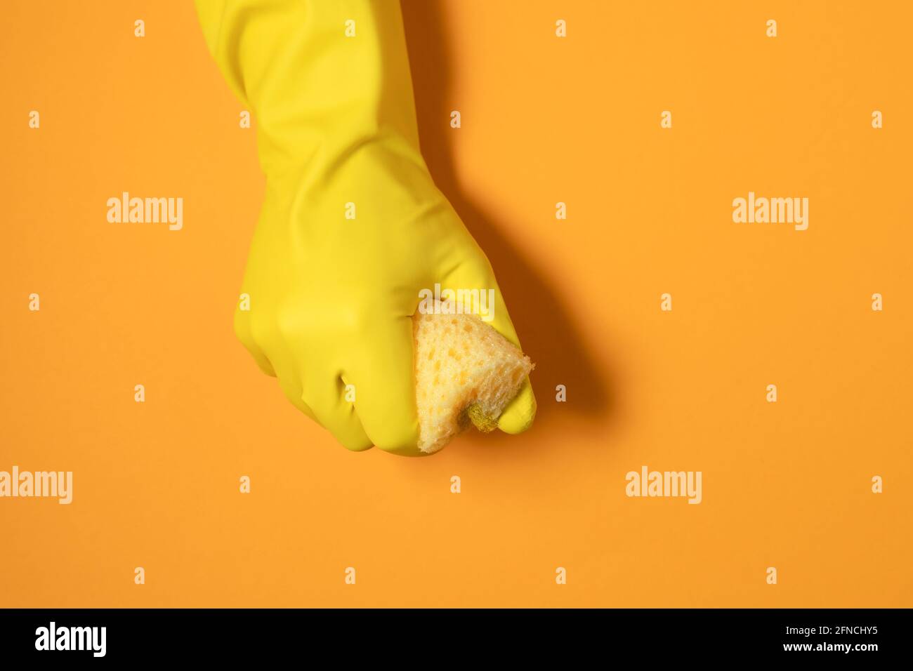 una mano en un guante de goma sostiene una esponja de limpieza. fotografía monocroma en colores amarillos. Foto de stock