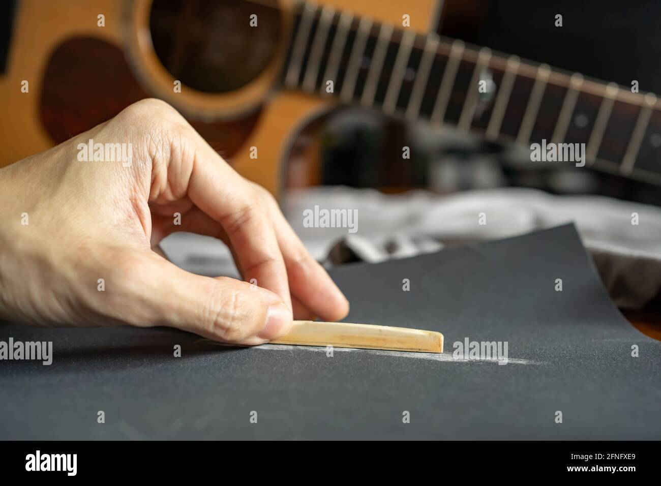 Baje la altura de una silla de guitarra acústica para un mejor jugabilidad  al lijar una silla de hueso con papel de lija Fotografía de stock - Alamy