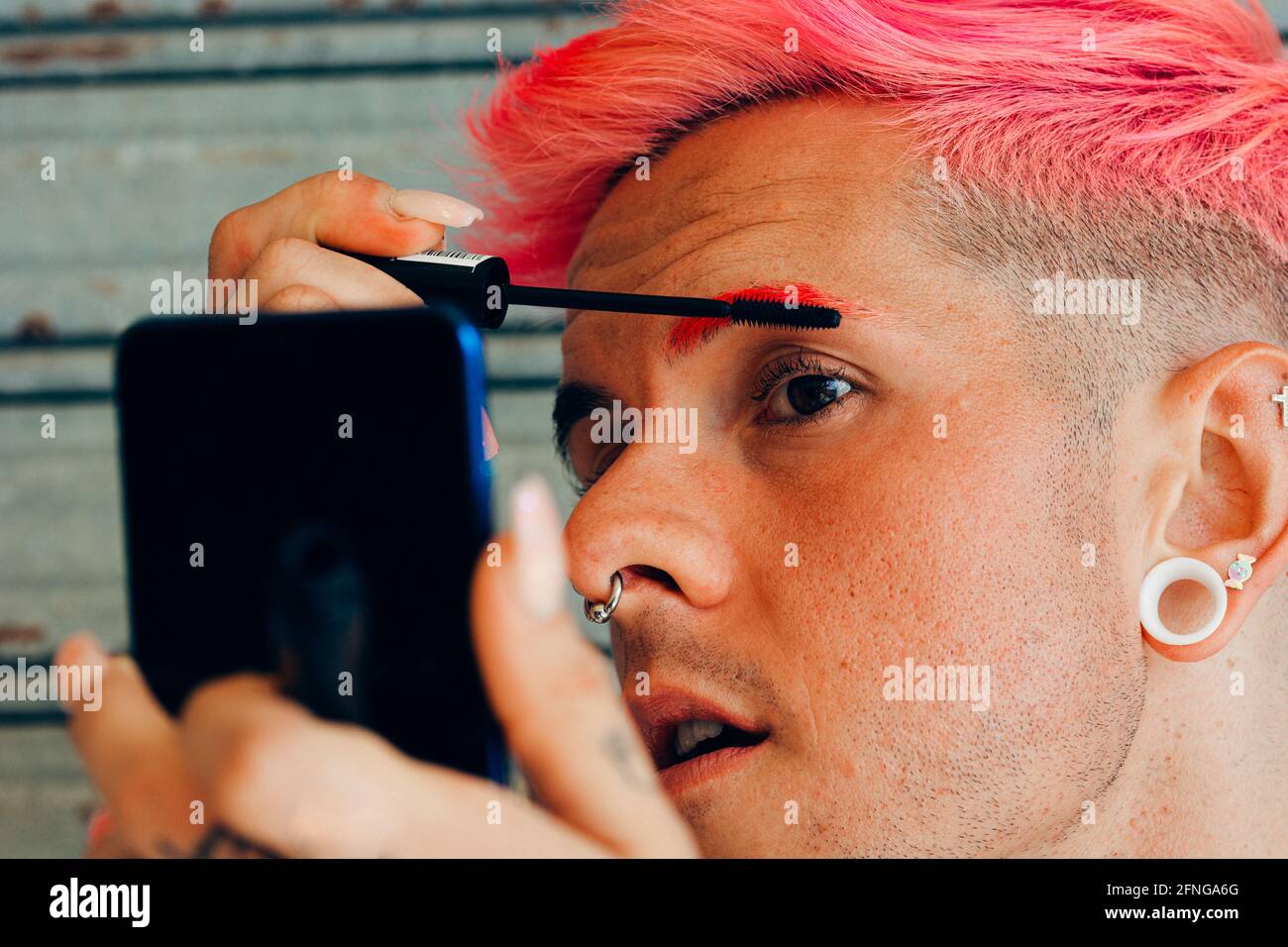 Hombre homosexual con piercings y corte de pelo moderno aplicando máscara  en pestañas con aplicador contra el teléfono móvil Fotografía de stock -  Alamy