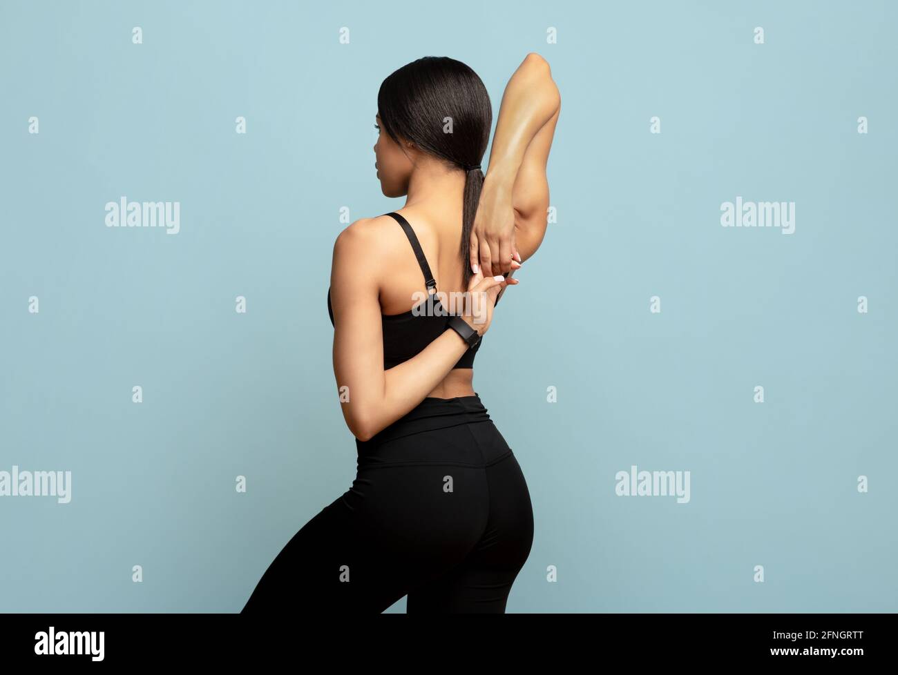Mujer negra joven en ropa deportiva calentándose antes del entrenamiento,  uniendo las manos detrás de su espalda sobre el negro azul del suelo  Fotografía de stock - Alamy