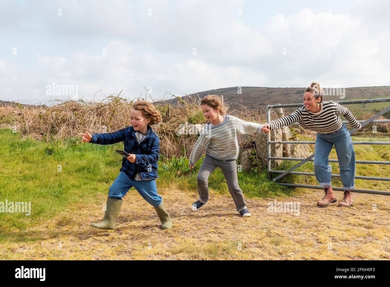 Una madre y sus hijos se divierten corriendo por un campo en la zona de West Penwith de Cornwall. Foto de stock
