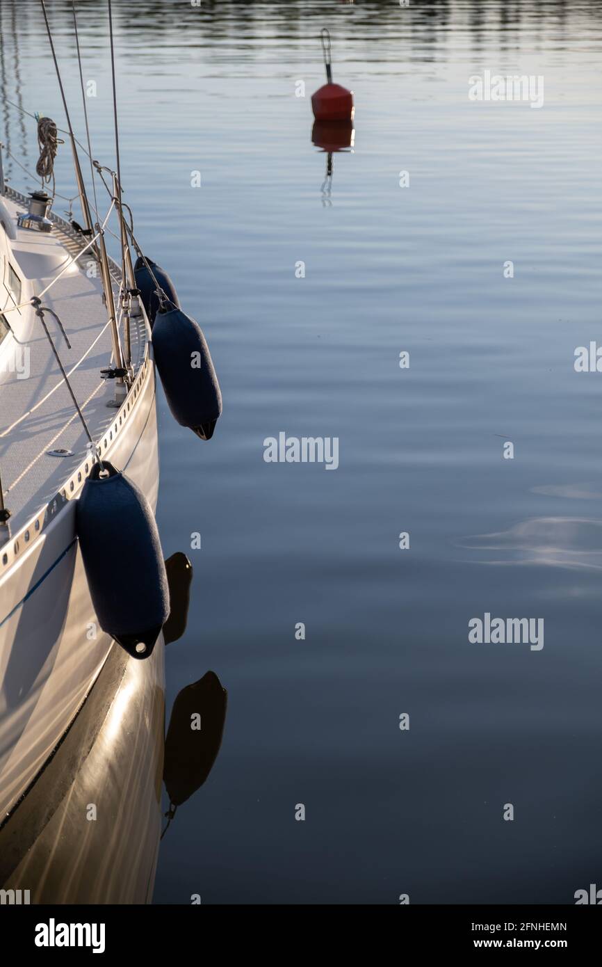 Helsinki / FINLANDIA - 16 DE MAYO de 2021: Un detalle de un casco de un barco de ocio. Guardabarros colgando en el barco que proyectan reflejos en el agua. Foto de stock