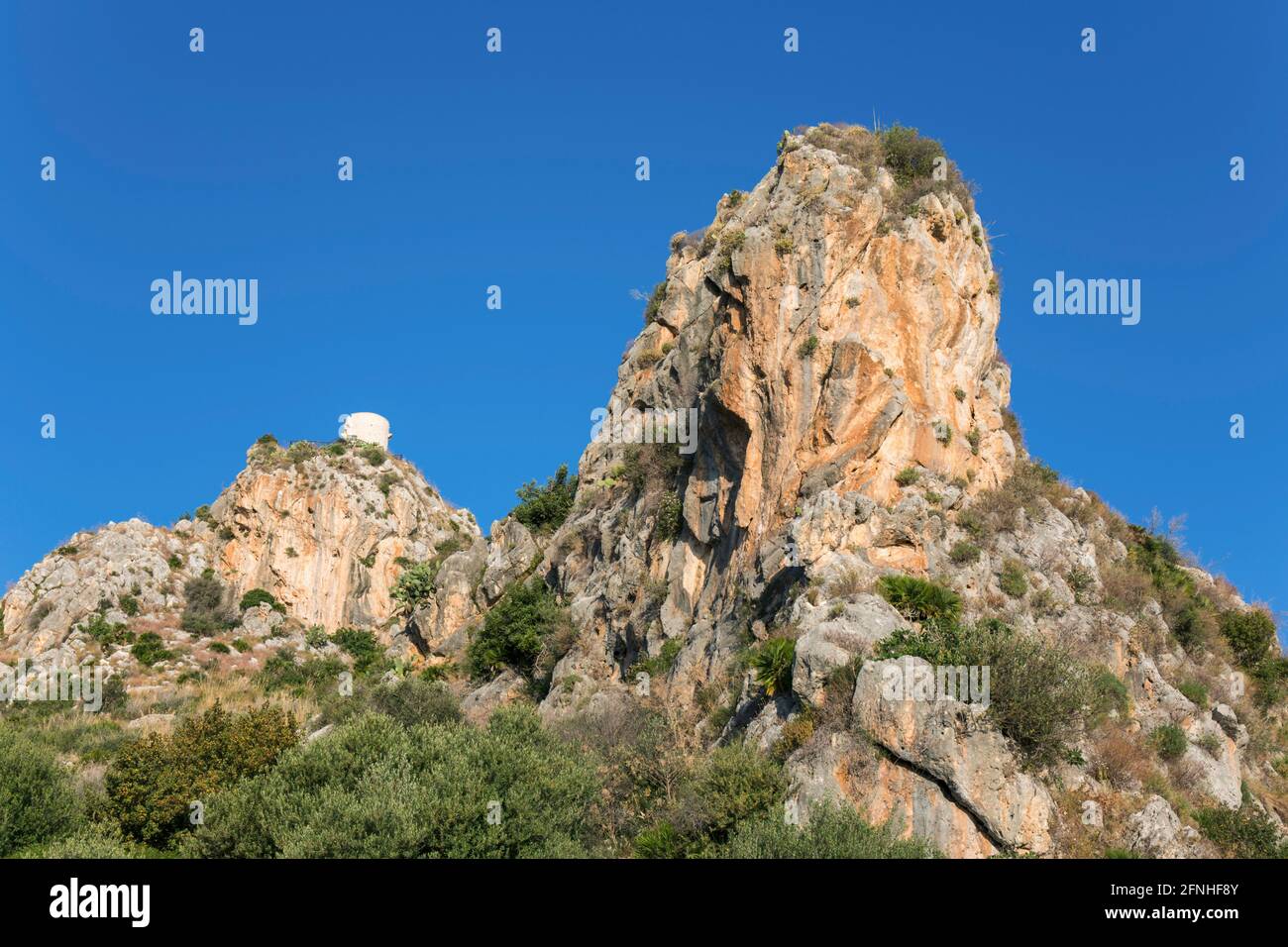 Scopello, Trapani, Sicilia, Italia. Vista de ángulo bajo desde el valle hasta la Torre Bennistra, una torre medieval restaurada, ahora un mirador acantilado. Foto de stock
