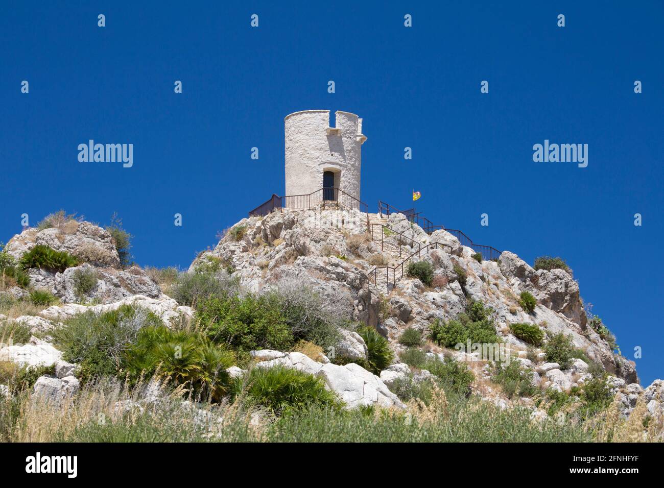 Scopello, Trapani, Sicilia, Italia. Vista a través de la ladera rocosa a la Torre Bennistra, una torre medieval restaurada, ahora un mirador acantilado. Foto de stock