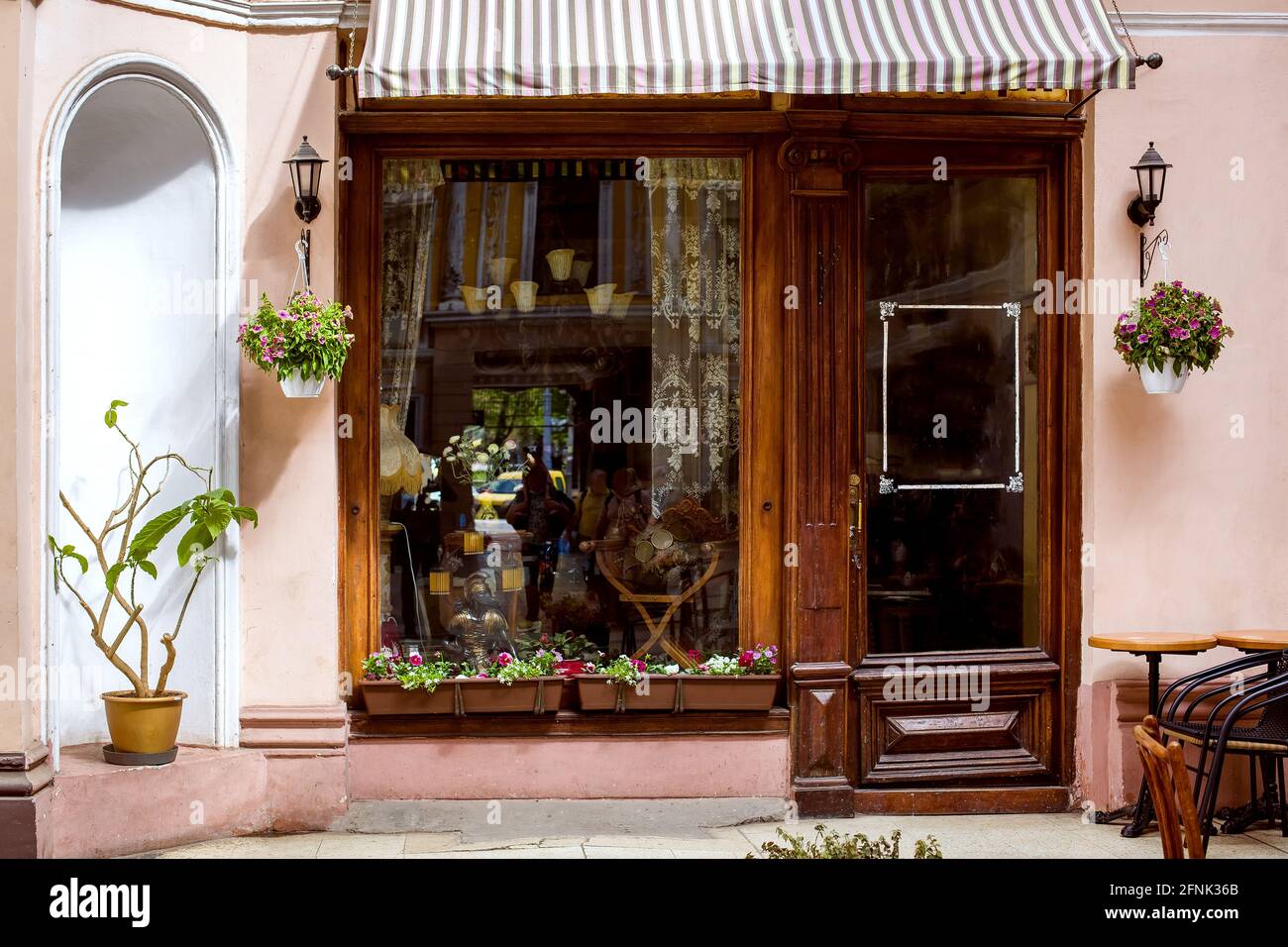 fachada de un café retro con una gran ventana y una puerta de madera con  cristal en la entrada, una mesa con sillas y macetas decorativas con flores  y Fotografía de stock -