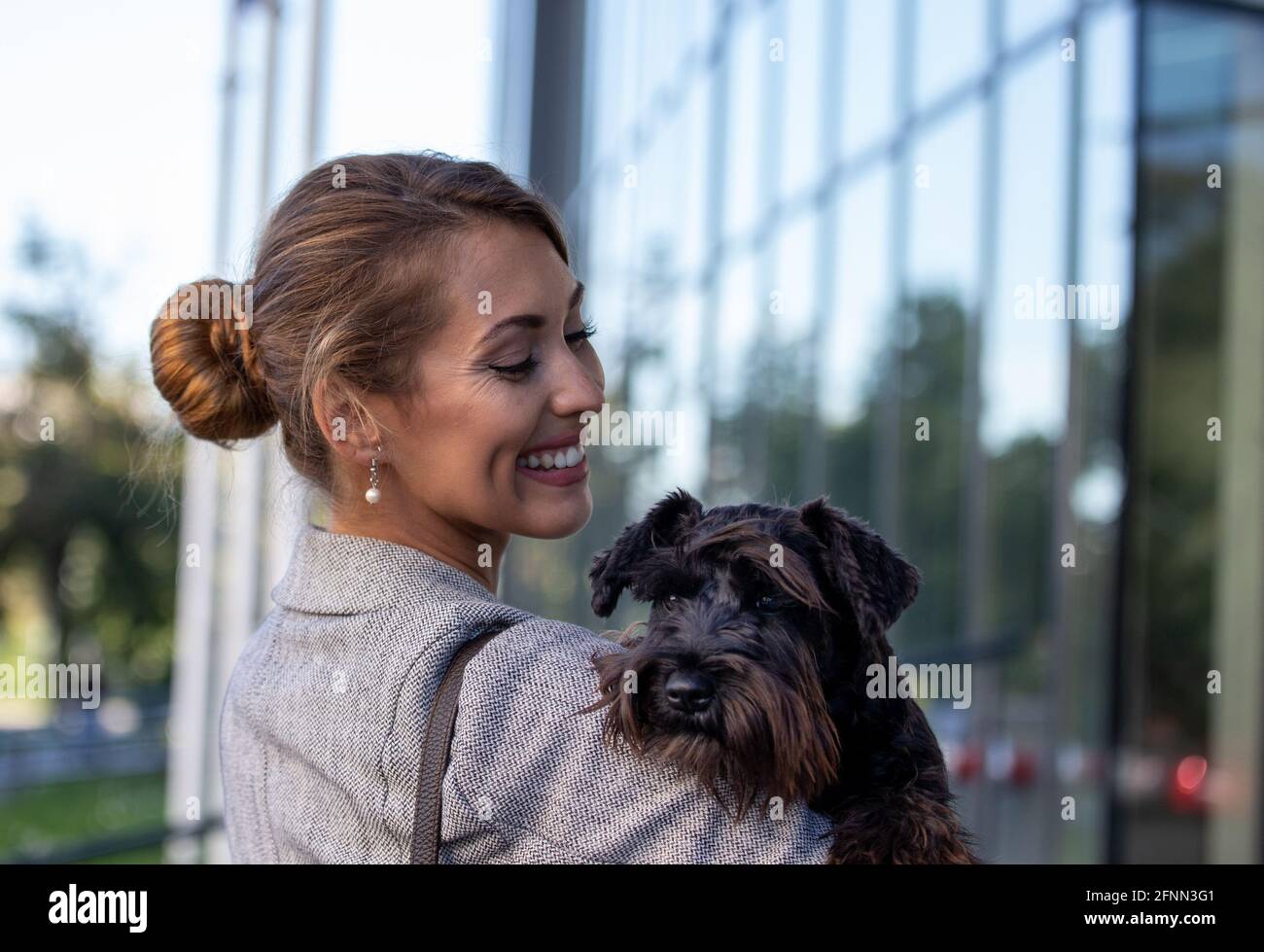 Bonita mujer de negocios joven sosteniendo lindo perro en los brazos frente del edificio de oficinas Foto de stock