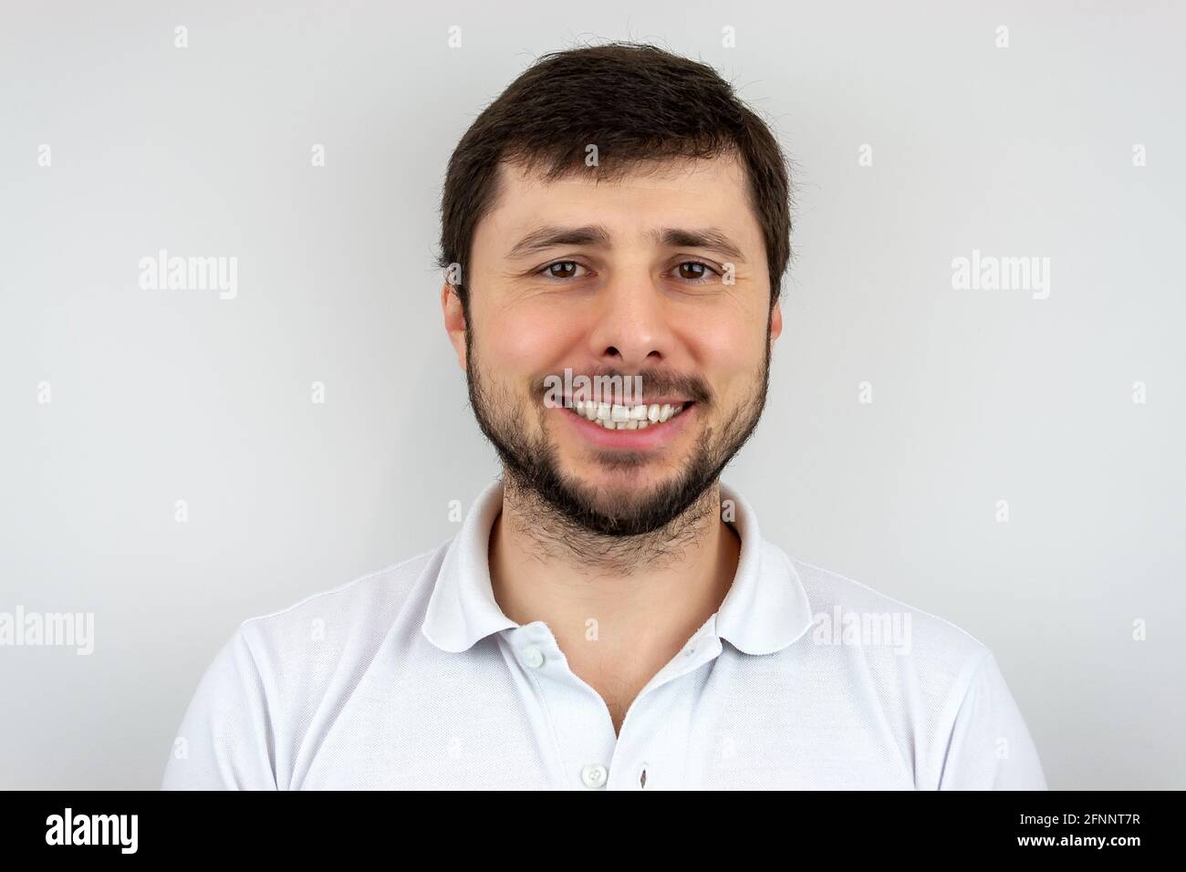 Un hombre barbudo muy feliz y sonriente con ojos marrones en una camiseta blanca Foto de stock