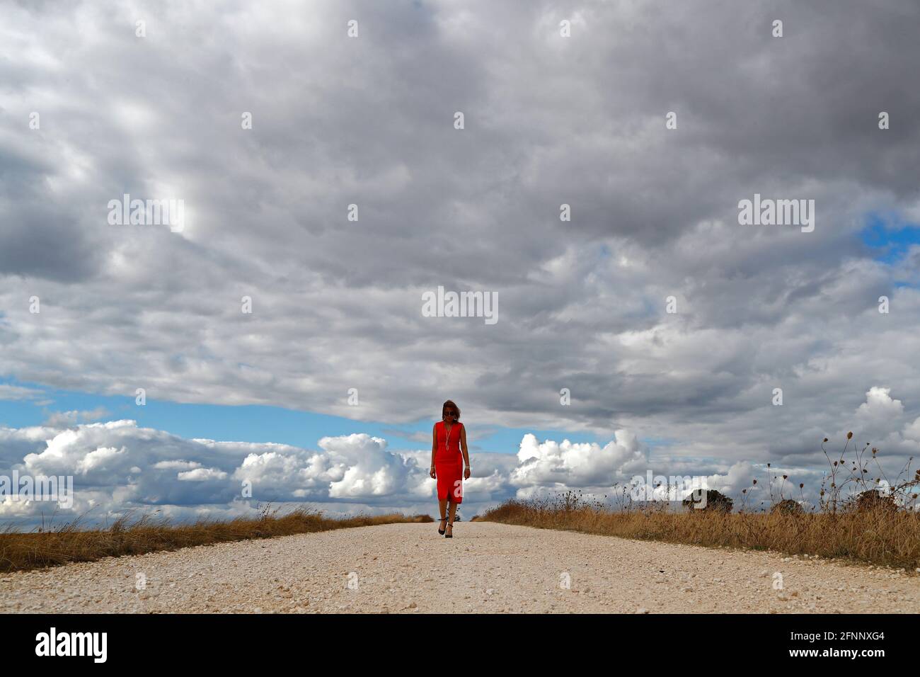 Mujer caminando sola por carretera recta. Cielo nublado. Francia. Foto de stock