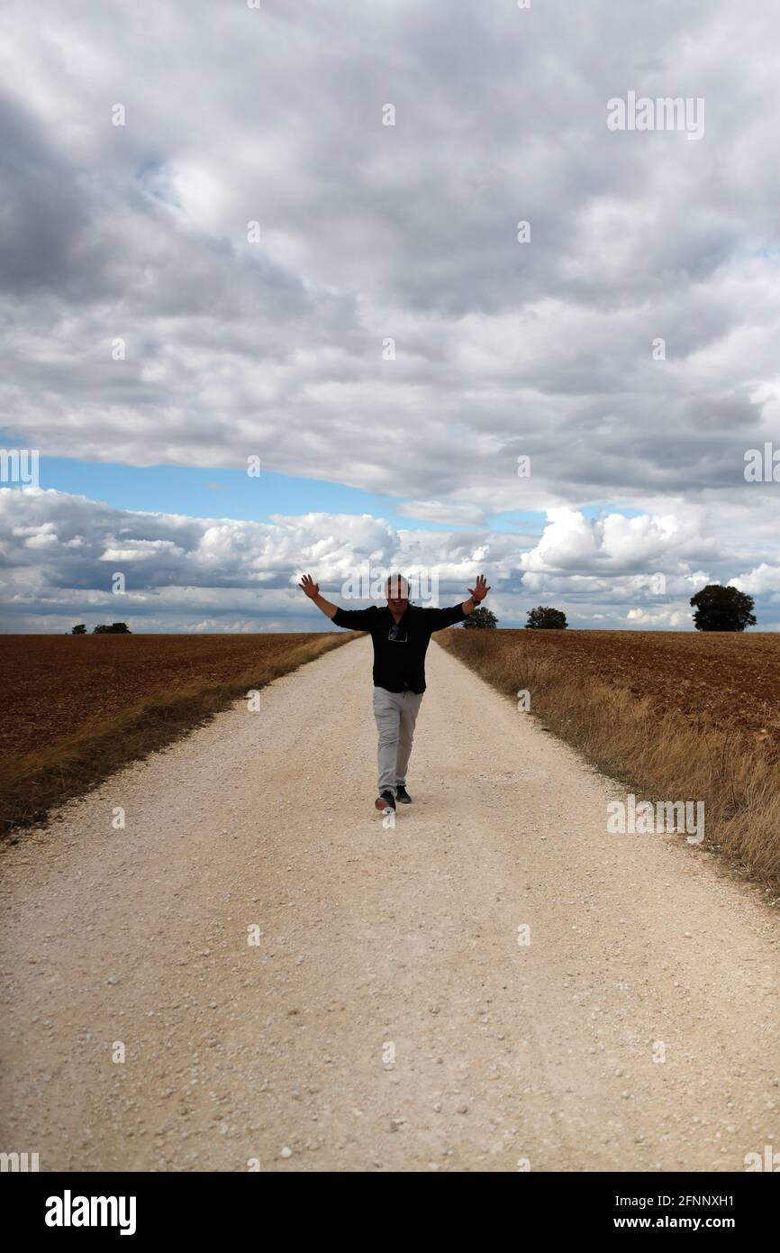 Hombre feliz caminando solo en la carretera de campo recta. Cielo nublado. Francia. Foto de stock