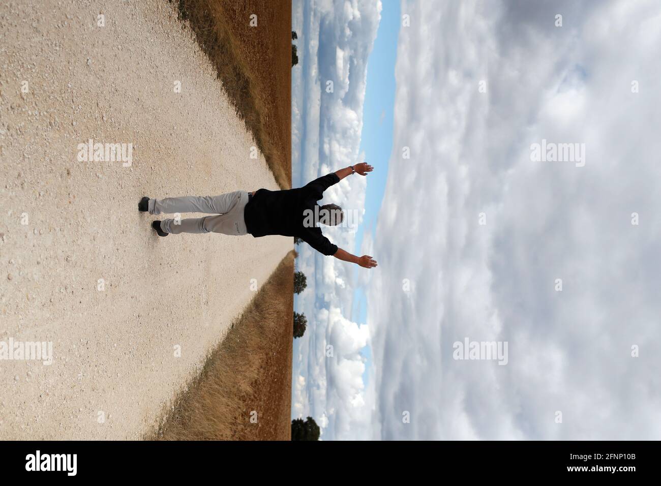 Hombre feliz caminando solo en la carretera de campo recta. Cielo nublado. Francia. Foto de stock