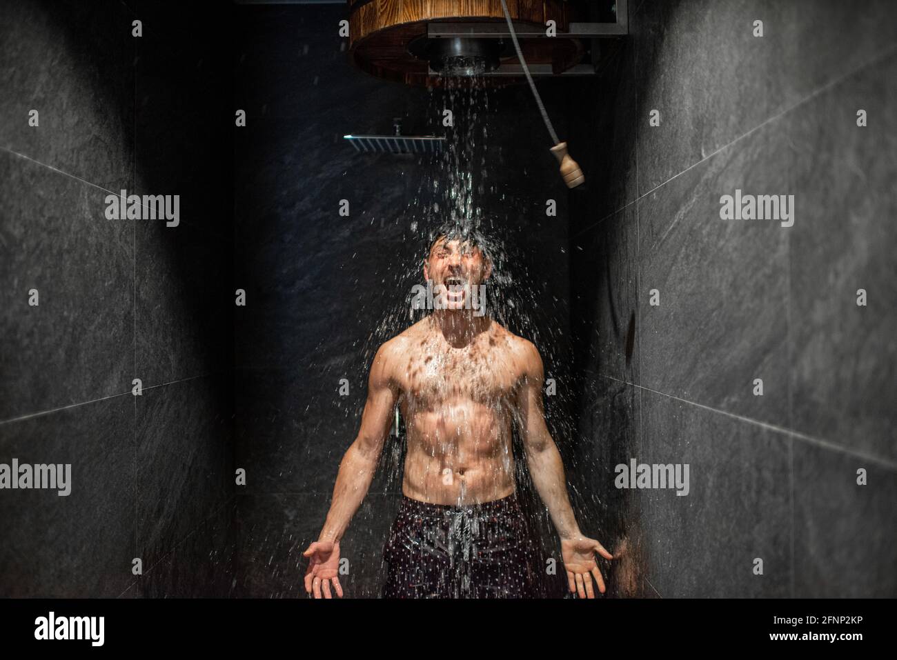 El hombre se endurece con un cubo de agua fría helada después de una sauna caliente, estilo de vida saludable y concepto de entrenamiento frío. Bienestar y spa. Foto de stock