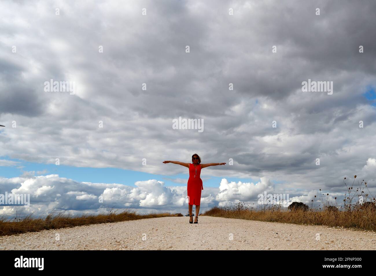 Mujer caminando sola por carretera recta. Cielo nublado. Francia. Foto de stock