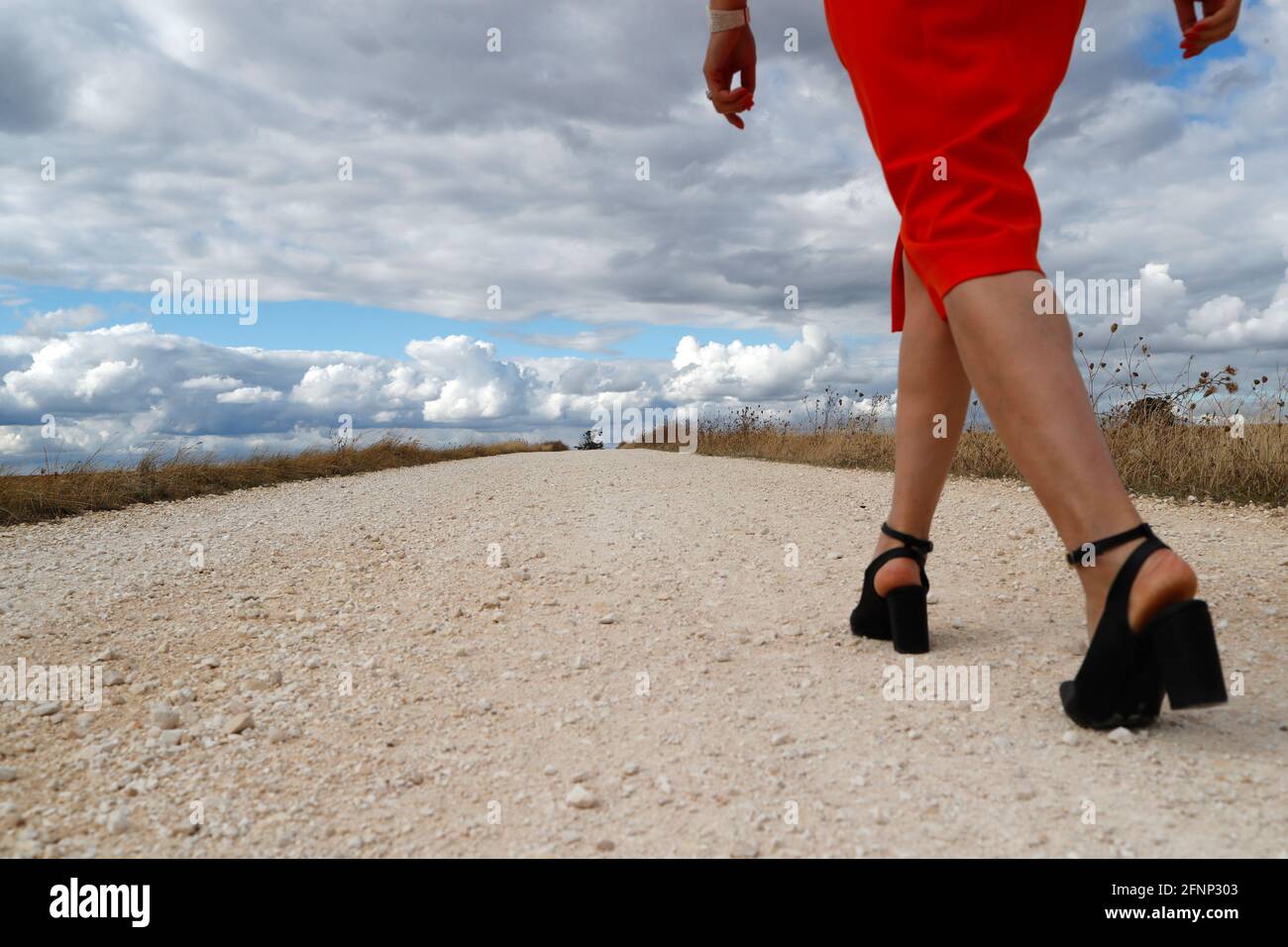 Vista trasera de una mujer caminando sola en la carretera de campo recta. Cielo nublado. Francia. Foto de stock