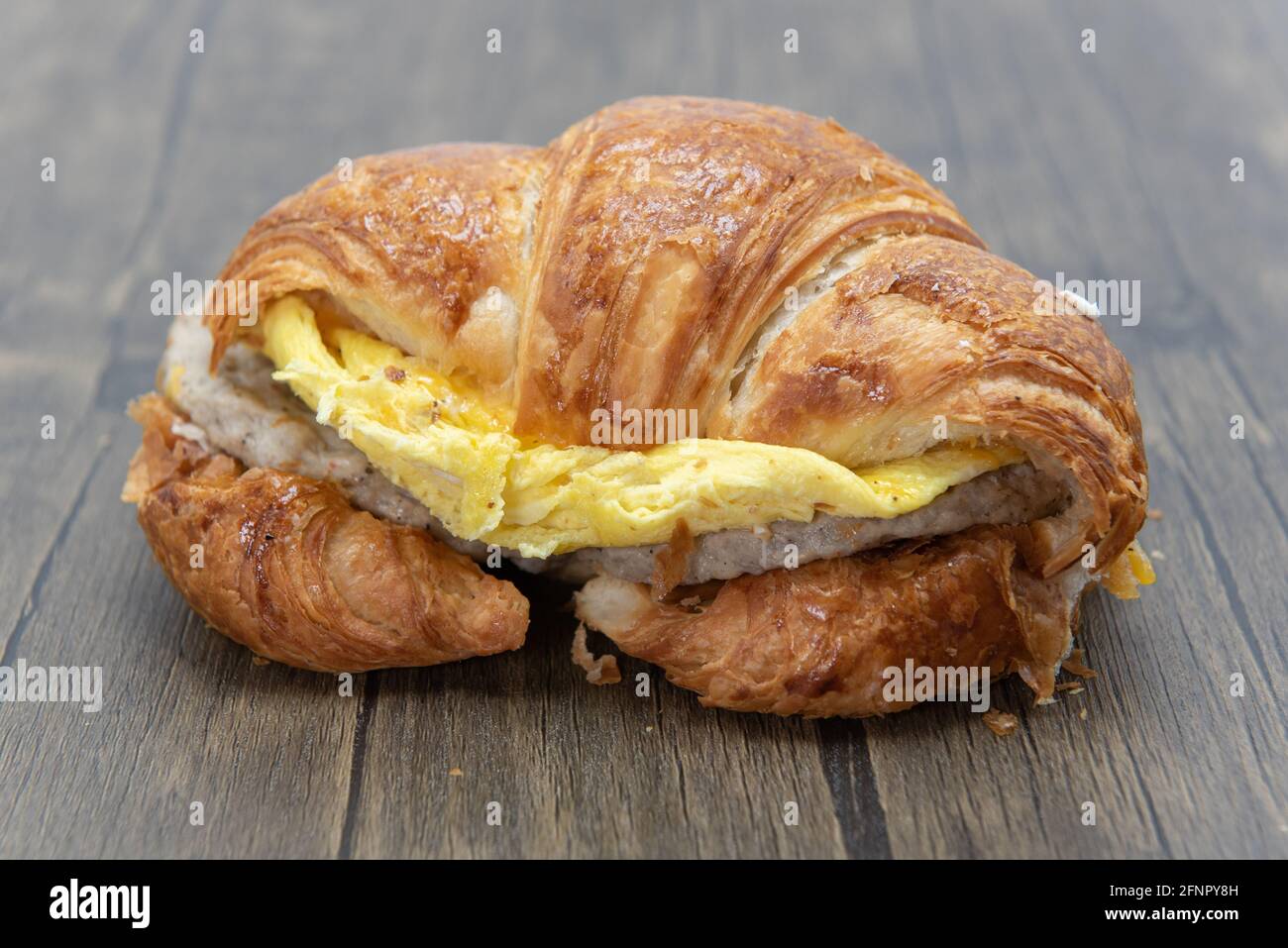 Delicioso sándwich de croissant cargado de huevos revueltos, queso fundido y empanada de