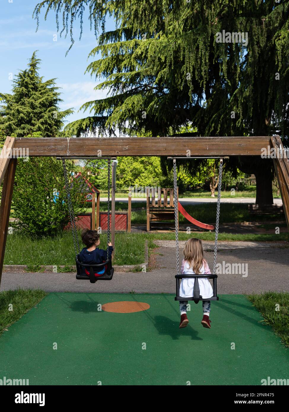 Dos niños juegan en un columpio en un parque público, fotografía callejera  con sujetos irreconocibles fotografiados desde atrás Fotografía de stock -  Alamy