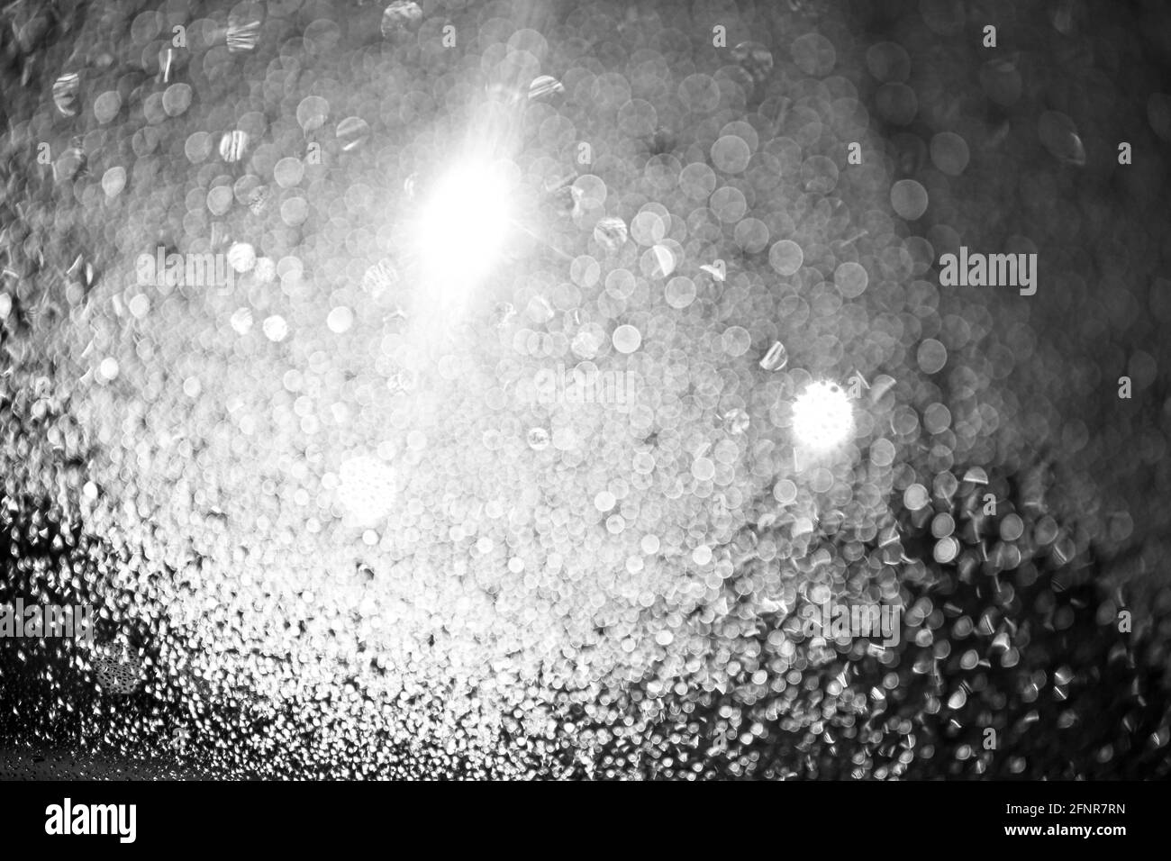 Gotas de lluvia en el vaso por la noche. Las linternas brillan. Bokeh blanco y negro. Cristal del coche. Desenfoque. Foto de stock