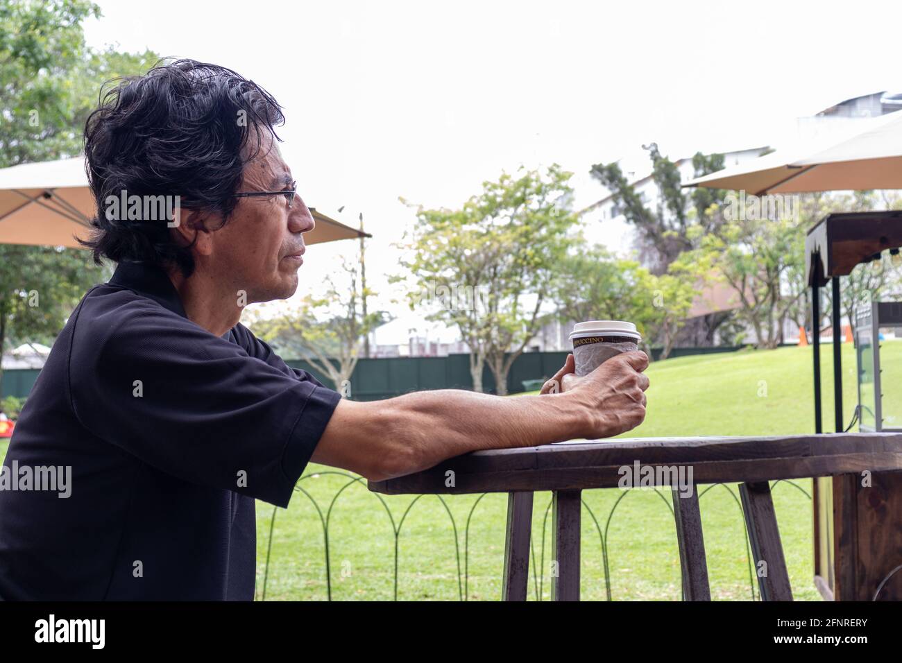 Hombre hispano usando una máscara facial en un parque bebiendo café Foto de stock