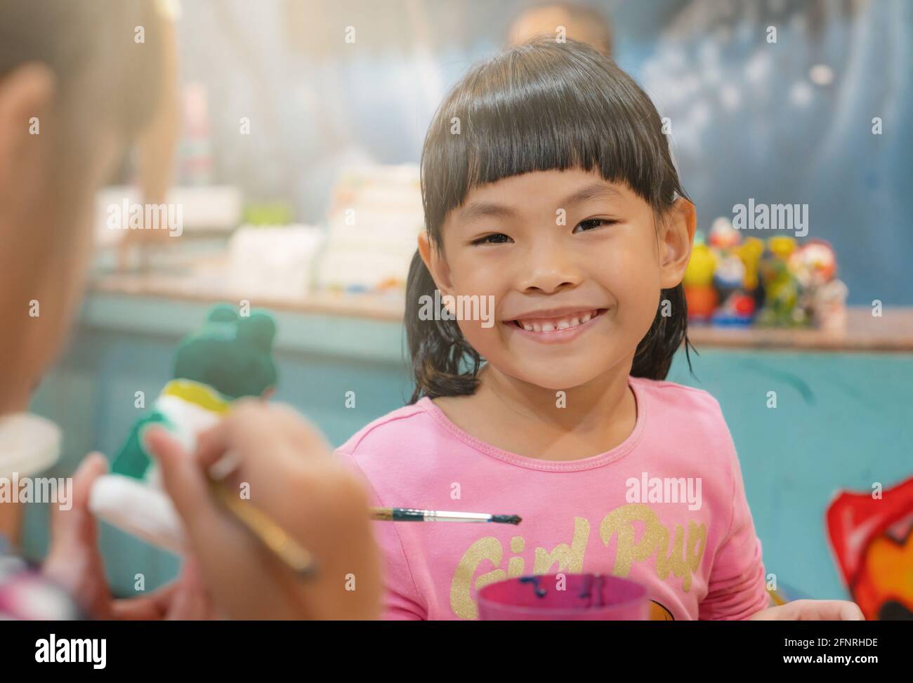 Retrato niña asiática en el taller de arte, cara feliz y sonriente, hermosa sonrisa, cara linda con pelo negro, y bang. Primer plano de clase borroso. Foto de stock