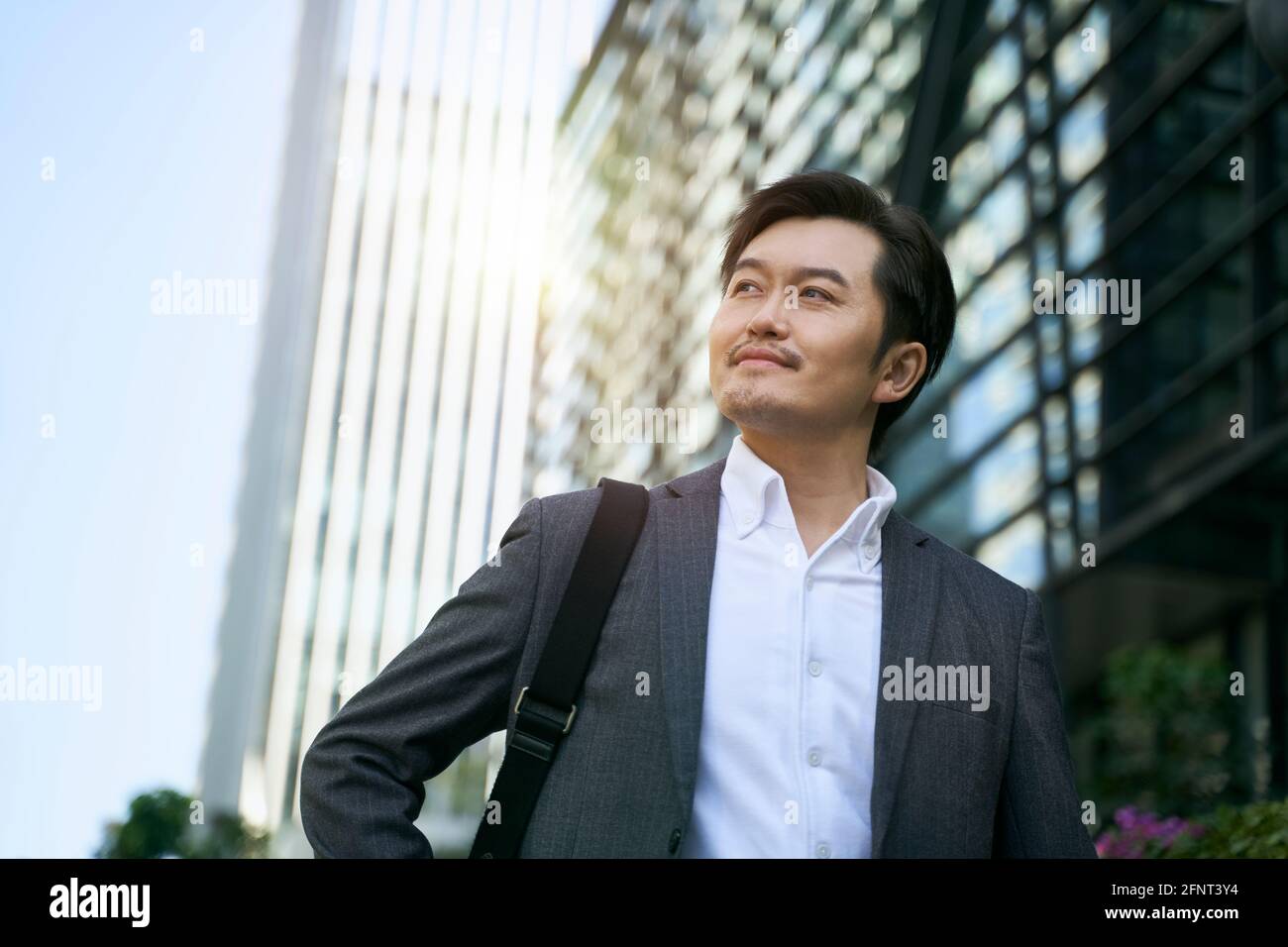 un ejecutivo corporativo asiático de éxito caminando en el distrito central de negocios de ciudad moderna Foto de stock