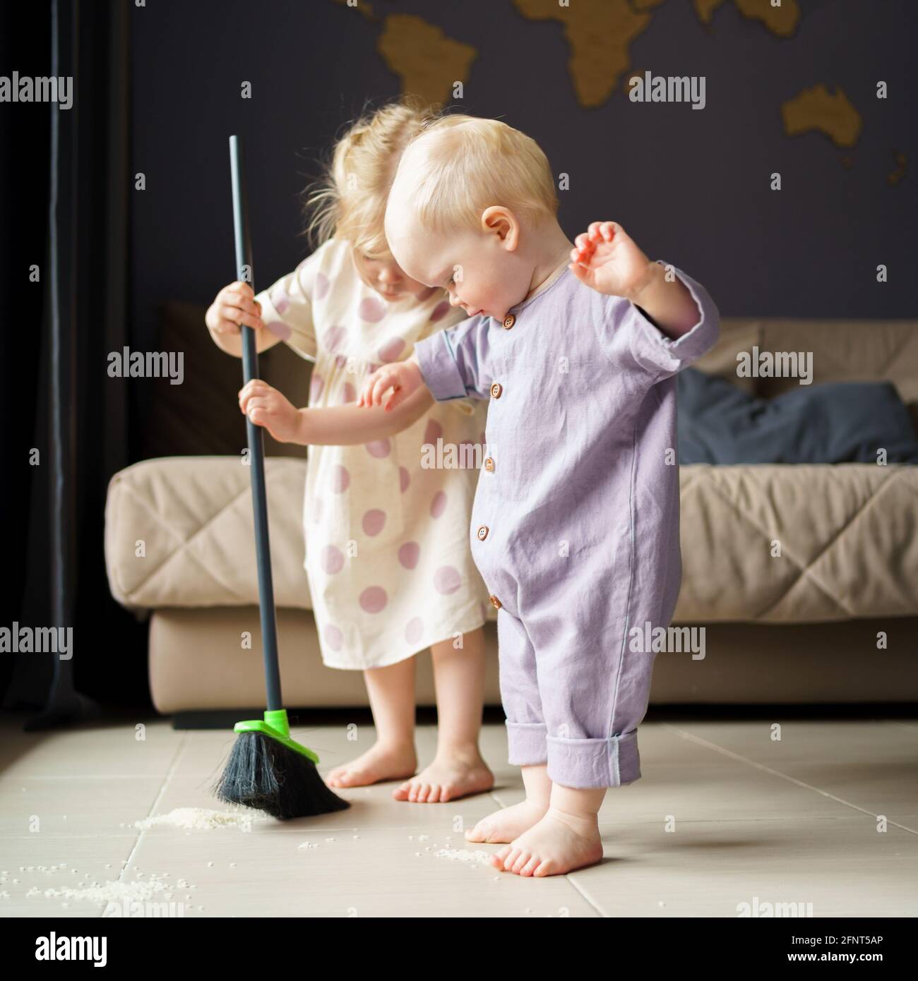 Lindos niño y niña ropa de cama barriendo el suelo en la habitación con escoba, ayudando a mamá con tarea de la casa en casa. El hermano del