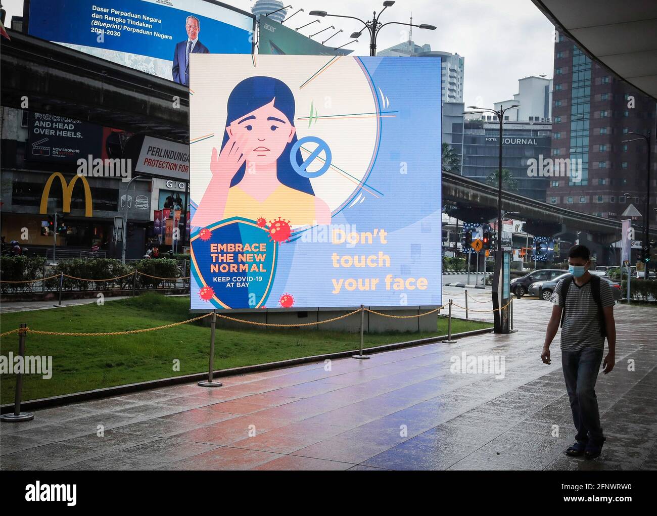 Kuala Lumpur, Malasia. 19th de mayo de 2021. Un hombre que lleva una máscara facial como medida preventiva contra la propagación del covid-19 camina por un cartel que dice 'No toque su cara'. Crédito: SOPA Images Limited/Alamy Live News Foto de stock