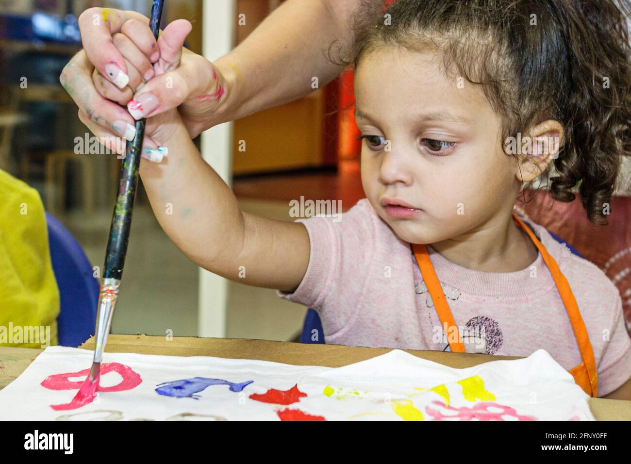 Miami Florida, Museo de los Niños camiseta taller de decoración, chica hispana niño niño niño pintura de la mano de los padres ayudar a guiar, Foto de stock