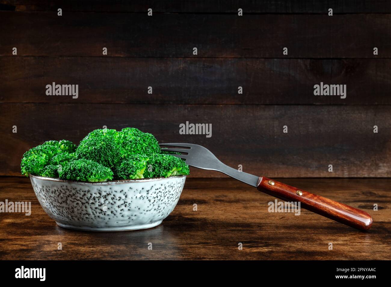 Cuenco de brócoli con un tenedor sobre un fondo rústico oscuro de madera con un lugar para el texto. Bandera de dieta vegetariana saludable Foto de stock