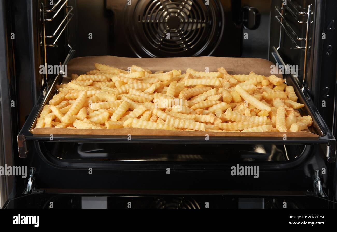 Bandeja con un montón de patatas fritas arrugadas abiertas horno durante la  preparación del almuerzo en cocina contemporánea Fotografía de stock - Alamy