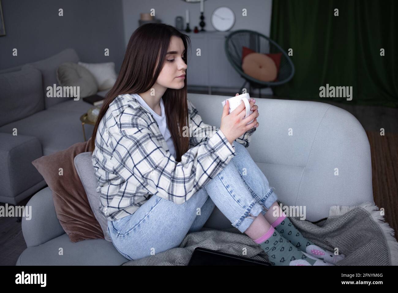Mujeres sentadas en un sofá acogedor con manta con café. La mujer se relaja disfrutando de un estilo de vida tranquilo en casa con una taza de té. Espacio de copia. Foto de stock
