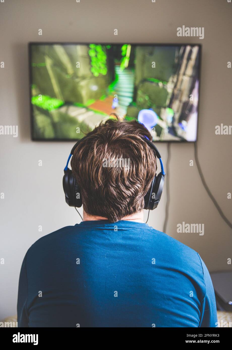 Vista trasera de un adolescente mirando la televisión mientras estaba jugar a videojuegos y usar micrófono y auriculares Foto de stock